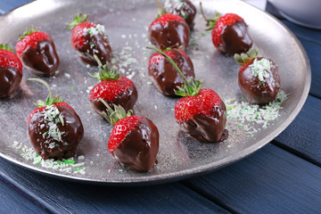 A plate of strawberries in chocolate on blue wooden background