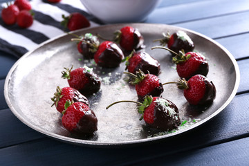 A plate of strawberries in chocolate on blue wooden background