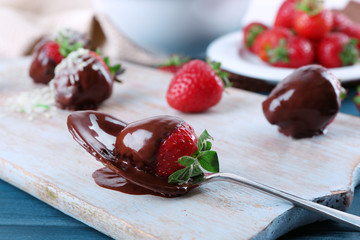 A spoon and delicious strawberries in chocolate on wooden tablet