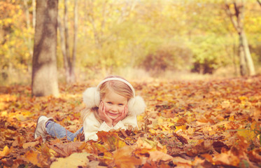 Little blonde girl portrait lying on autumn yellow maple leaves outstretched hands and smiling.