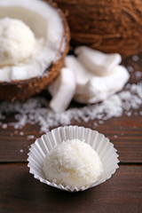 Candies in coconut flakes and fresh coconut on dark wooden background