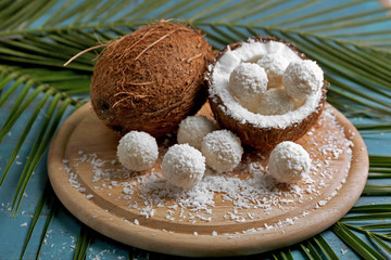 Candies in coconut flakes and fresh coconut on color wooden background