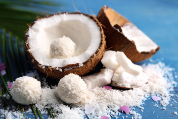 Candies in coconut flakes and fresh coconut on color wooden background