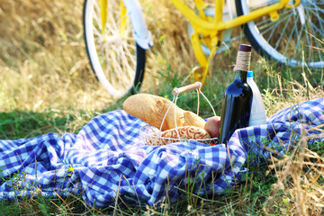 Old yellow bicycle and picnic snack on checkered blanket on grass in park