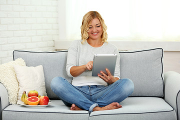 Fototapeta premium Beautiful woman with fresh fruits and digital tablet on home interior background