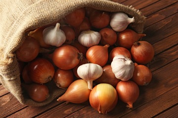 Scattered sac with fresh onions and garlic on wooden background