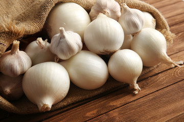Scattered bag with onions and garlic on wooden background