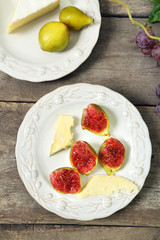 Ripe figs and cheese on plate, on wooden background