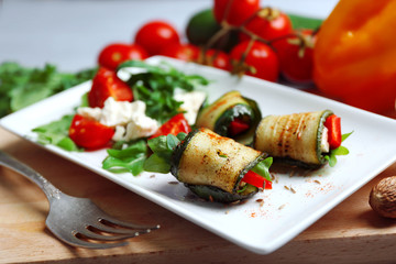 Zucchini rolls with cheese, bell peppers and arugula on plate, close-up, on table background