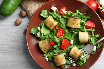 Salad with arugula and zucchini rolls on plate, on table background