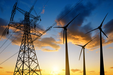High voltage tower and wind turbines against the sunset