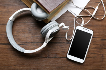 Headphones with old book and smartphone on wooden table