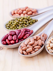 Assortment of beans and lentils in wooden spoon on wooden backgr