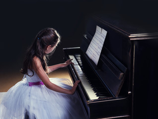 Cute little princess girl plays piano in the dark room