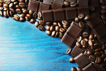 Black chocolate pieces and coffee grains on color wooden background