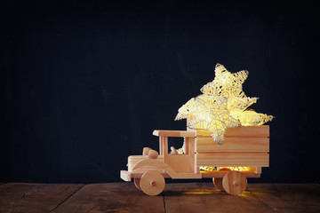 low key image of retro wooden toy car with garland golden stars over wooden table. nostalgia and simplicity concept. retro style image.