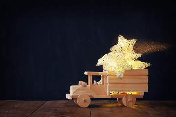 low key image of retro wooden toy car with garland golden stars over wooden table. nostalgia and simplicity concept. retro style image.