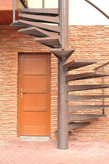 Metal winding stairs at red slate wall.