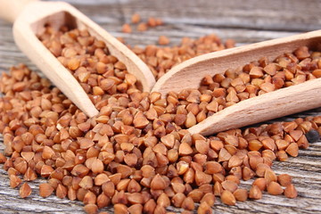 Heap of buckwheat groats with spoon on wooden surface