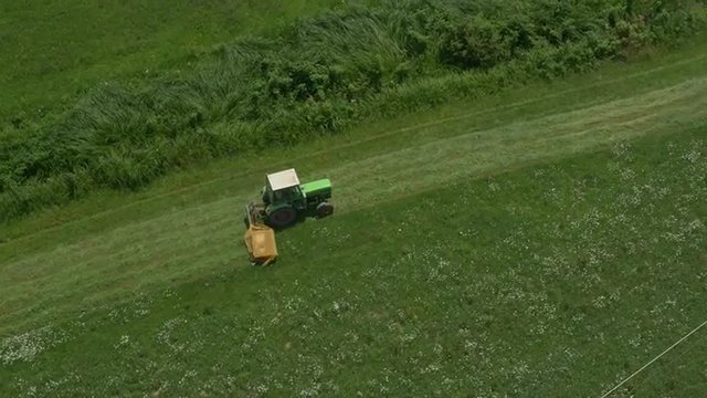 AERIAL: Tractor mowing in a big grass field