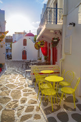 Mykonos streetview at sunrise with chapel and yellow chairs and tables, Greece