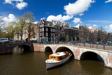 Amsterdam canal intersection with white boat in summer with a blue sky - obrazy, fototapety, plakaty