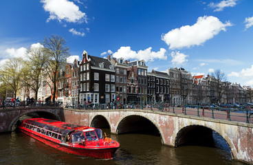 Amsterdam canal intersection with red cruise boat in summer with a blue sky