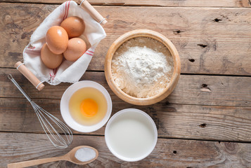 The flour in a wooden bowl, egg, milk and whip for beating.