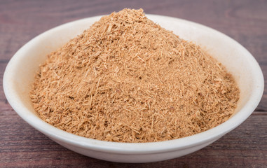 Dried galangal powder in white bowl over wooden background