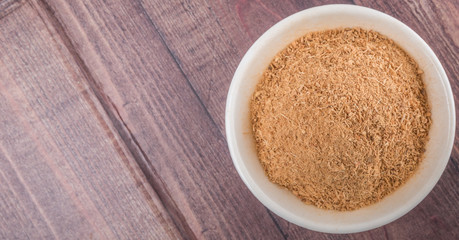 Dried galangal powder in white bowl over wooden background