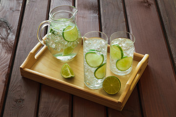 Two drinks and jug on wooden tray with ice and condensation on g