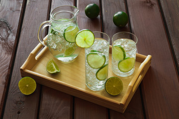 Two drinks and jug on wooden tray with ice and condensation on g