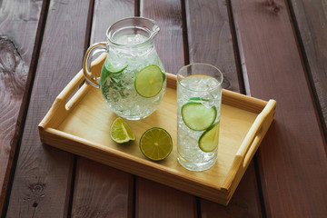 Drink and jug on wooden tray with ice and condensation on glass