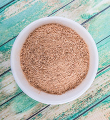 Dried galangal powder in white bowl over wooden background