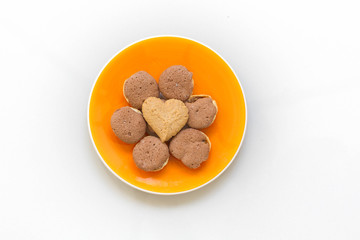 Chocolate cookies and butter cookies heart shape on orange dish on white background