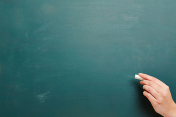 Hand mit Kreide vor gr&uuml;ner Kreidetafel
