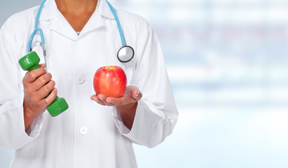 Doctor woman hands with dumbbell and apple.