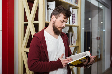 Fototapeta premium Concentrated guy holding glasses and reading book in library
