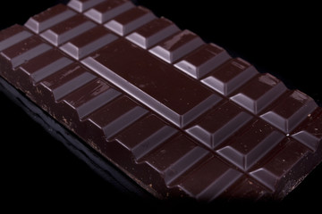 Tiles of black chocolate on black glossy background