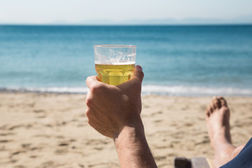 Hand holding glass of beer on seacoast - 95114471