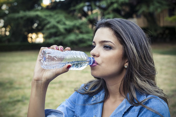 Beautiful girl sitting on the bench drinking water
