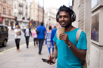 young man in the street with a coffee, headphones and mobilephone