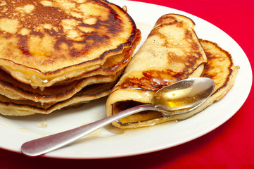 delicious pancakes with honey sauce on red background