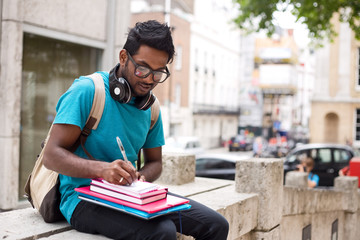 student sitting outdoors writing in a textbook