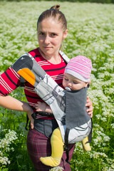 Mama with a small child in her arms, walking in a green field in summer colors.
