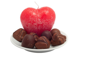 red heart-candle and chocolate sweets on a white saucer separate