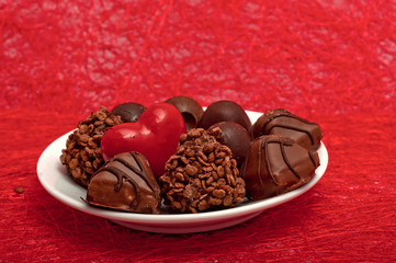 red heart and chocolates on a white saucer on red sisal