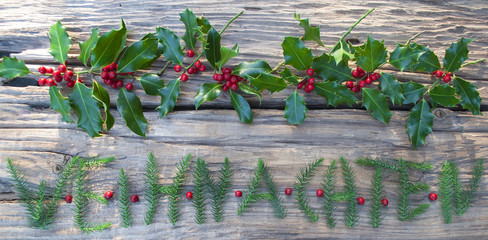 Schriftzug Weihnachten mit Tannenzweigen und Ilex / Stechpalme auf altem Treibholz / Holzbrett 
