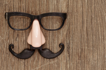 fake mustache, nose and eyeglasses on a wooden surface