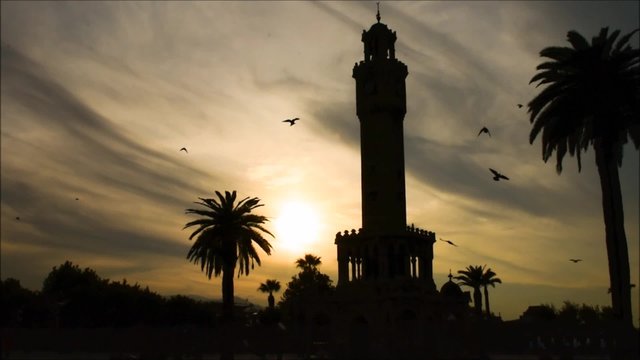 Historical clock tower  silhouette at sunset,  Izmir ( Smyrna ) - Turkey. Birds flying around - slow motion 